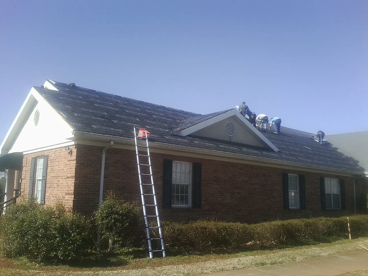 Crew tearing shingles off a brick ranch roof with a ladder set — Metal Roof Repair work by our crew in Hereford